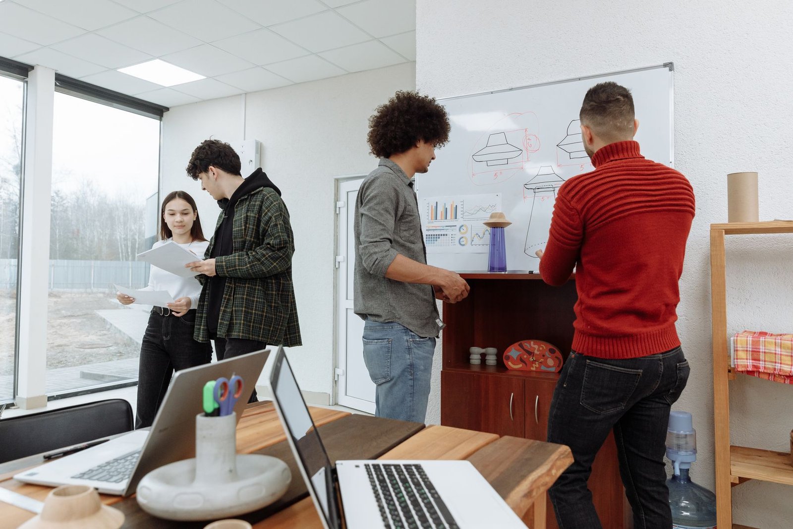 Young professionals collaborating with laptops and a whiteboard in a modern office