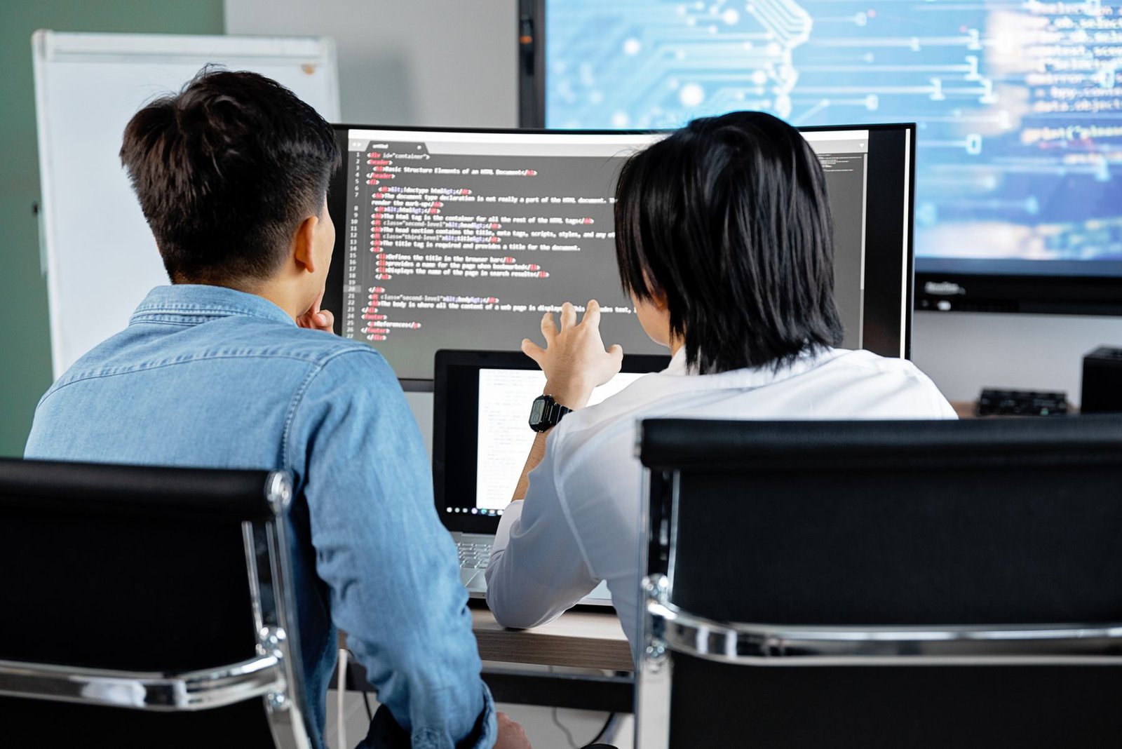 Two software developers collaborating on code at a shared computer in a modern office